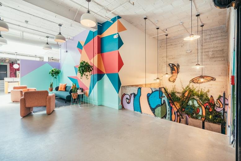 Spacious communal lounge with colorful geometric wall murals, plush armchairs, and hanging pendant lights.