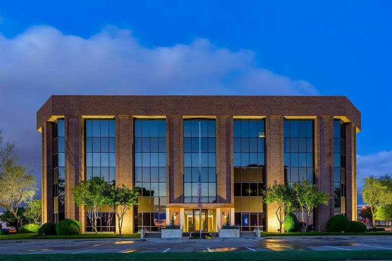 Exterior view of the brick and glass office building at 13465 Midway Rd during twilight.