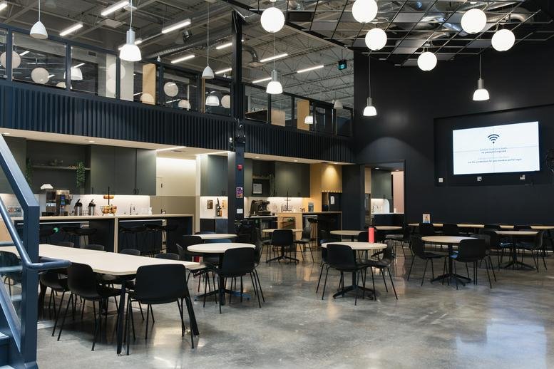 Spacious communal lounge at 137 Glasgow St, Suite 210, Kitchener with a cafe, tables, and a large media screen.