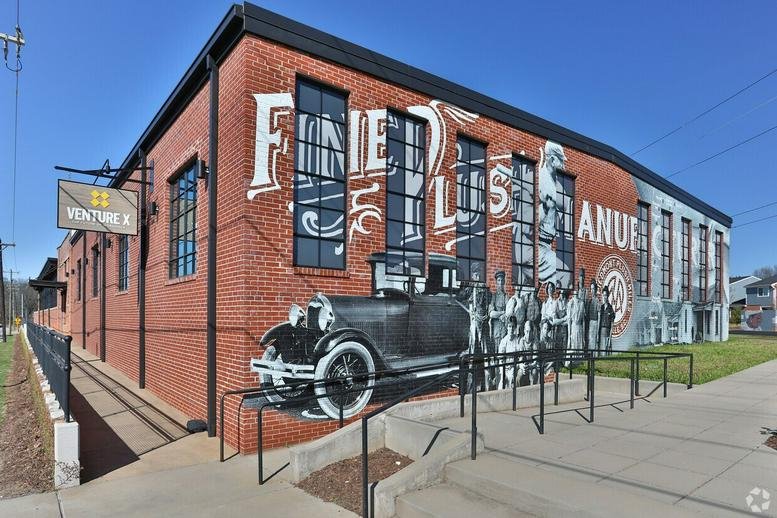 Exterior brick facade of the Venture X at 141 Traction Street featuring large industrial windows and a vintage mural.