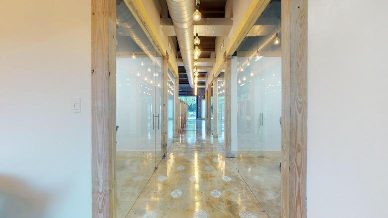 Bright hallway at 142 NW 37th St with wooden-framed glass office suites and polished concrete floors.
