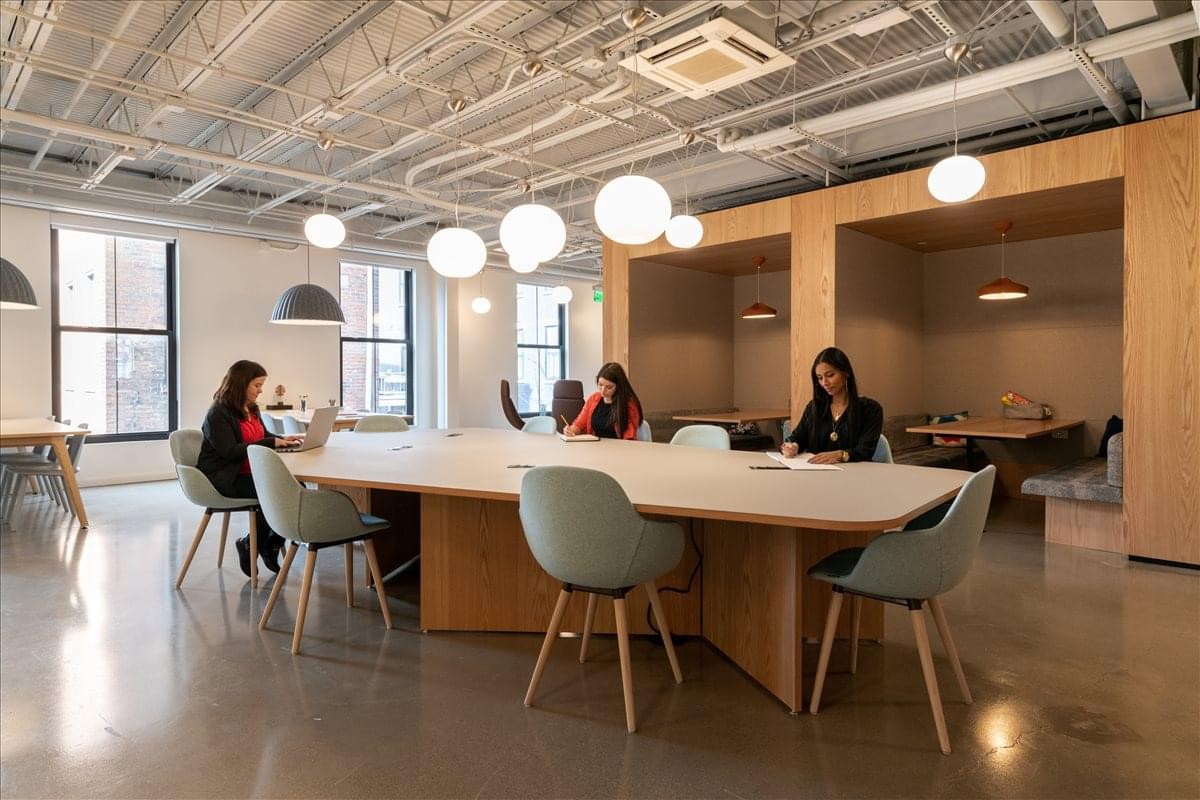 Spacious coworking area with a long white table, globe pendant lights, and industrial ceilings.