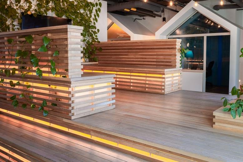Spacious communal lounge at 150 Elgin Street featuring wooden seating, warm lighting, and climbing wall plants.