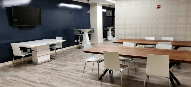 Flexible training or event space with long wooden tables and white chairs.