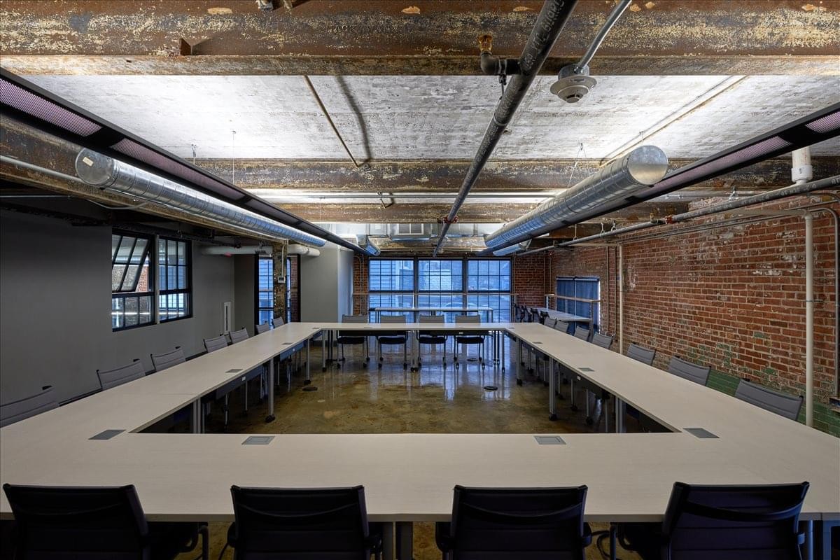 Spacious boardroom at 155 Chandler St featuring a large square table and exposed industrial ceilings.