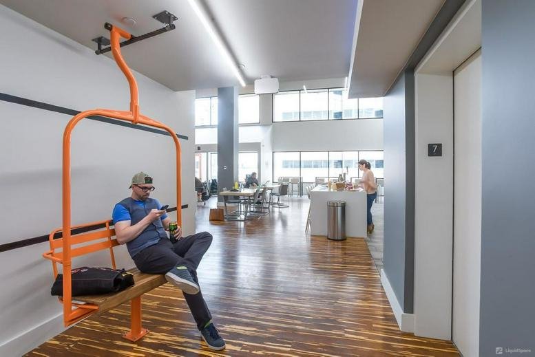 Spacious coworking area at Strive Denver featuring a quirky orange ski lift chair and warm wood floors.