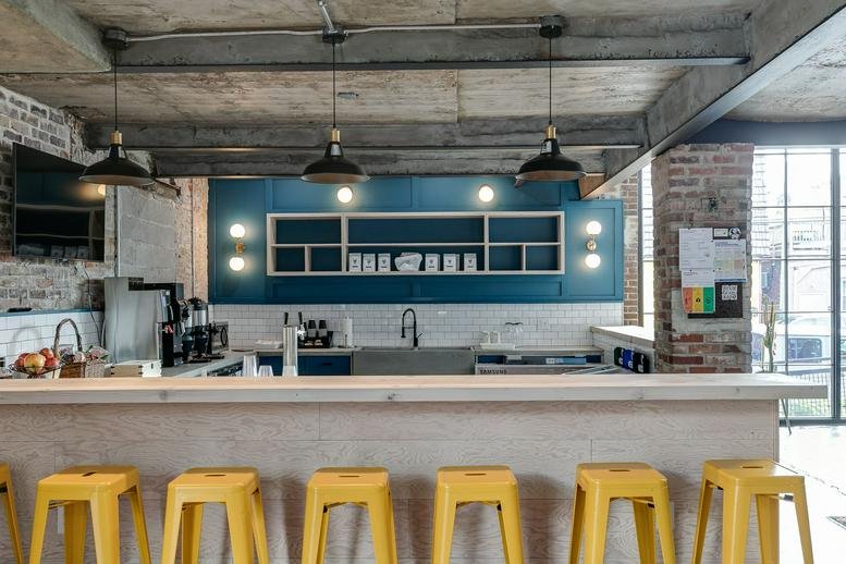 Modern communal kitchen with teal cabinetry and yellow stools at 1727 Snyder Avenue.