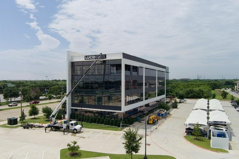 Wide exterior view of the glass-facade building with a large parking lot and surrounding greenery.