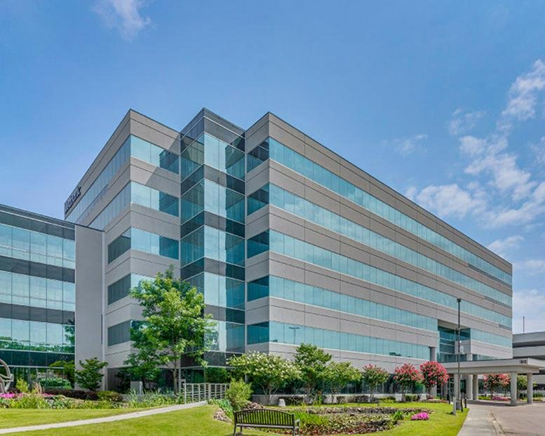 Wide view of the glass office building exterior with landscaped gardens and bright blue sky.