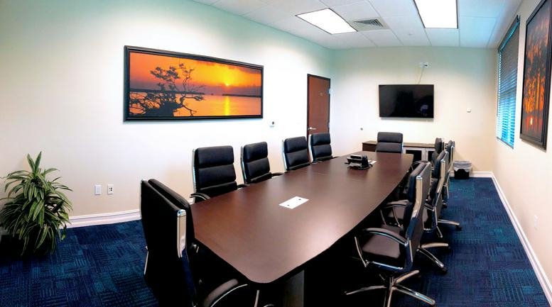 Spacious boardroom with a large dark wood table, leather chairs, and a scenic sunset mural.