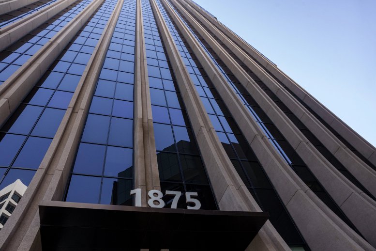 Looking up at the glass and stone facade of 1875 Century Park E against a clear blue sky.