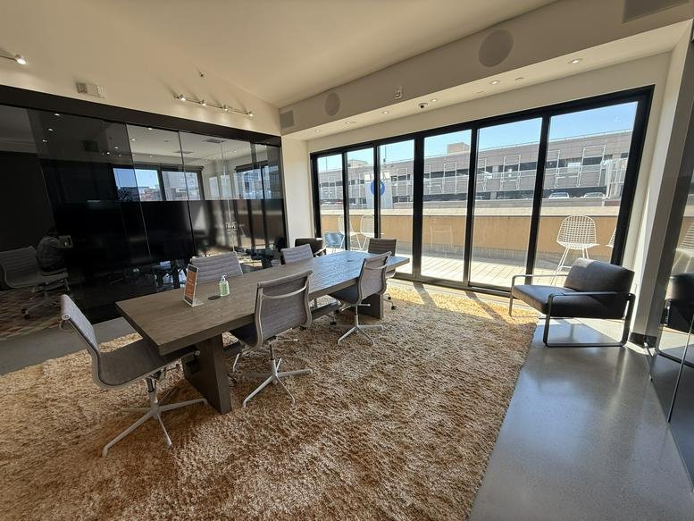 Meeting area with a grey wooden table over a tan shaggy rug and large sliding glass doors.