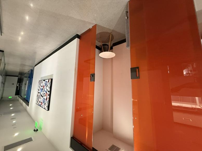 Modern phone booth with orange glass doors and an abstract painting nearby.