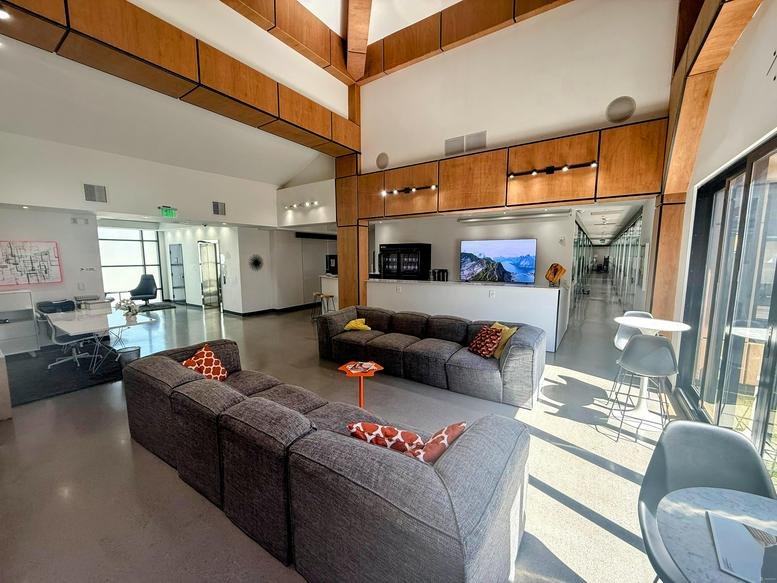 Bright lobby lounge with large grey sectional sofas, wood paneling, and polished concrete floors.