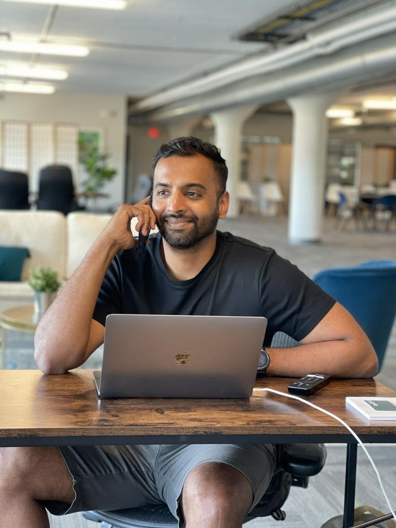 A man using a laptop and phone at a wooden desk in the bright office space at 201 North Main Street, 4th Floor.