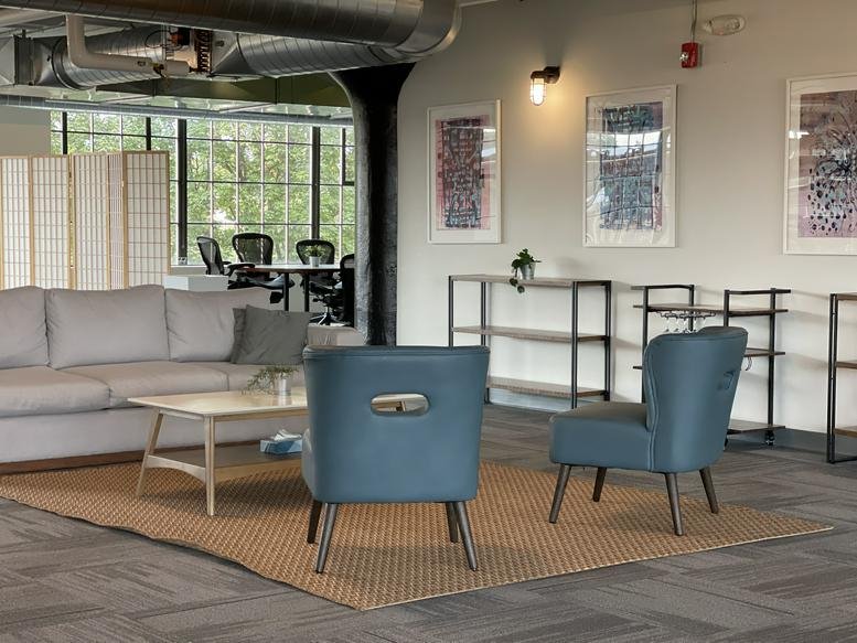 Spacious lounge area with a grey sofa, blue armchairs, and framed art pieces.