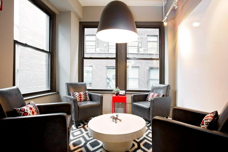 Lounge area with black armchairs, patterned rug, and large windows at 21 West 46th Street.