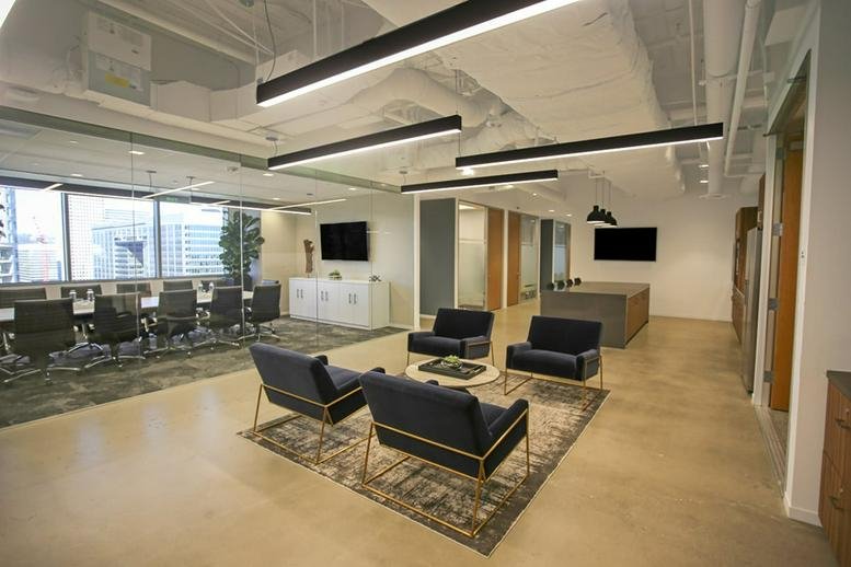 Bright lounge space with blue armchairs, patterned rug, and view of a large boardroom.