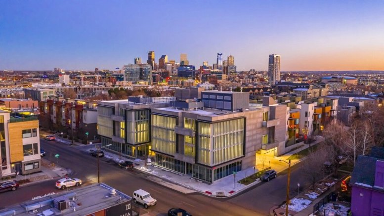 Dusk aerial view of the illuminated office building with the city skyline behind.