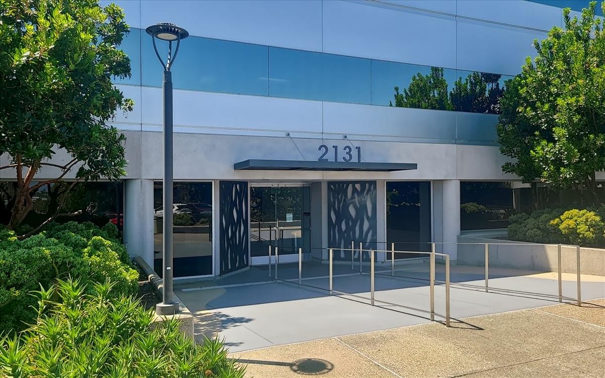 Exterior entrance and facade of 2131 Palomar Airport Road with glass windows and manicured hedges.