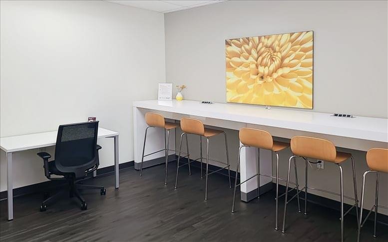 Collaborative breakout space featuring a long white high-top table and orange stools.