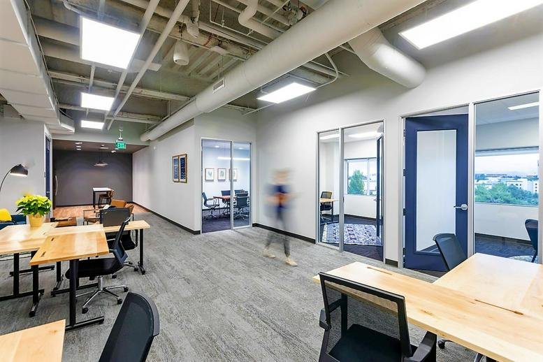 Modern hallway with glass-partitioned offices and exposed ceiling pipes.