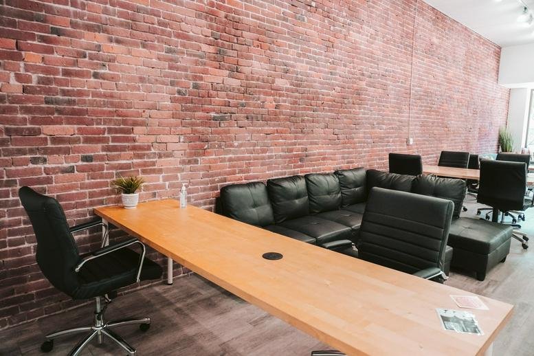 Spacious communal coworking area at 216 Commercial Street North East featuring a long wooden desk and brick wall.