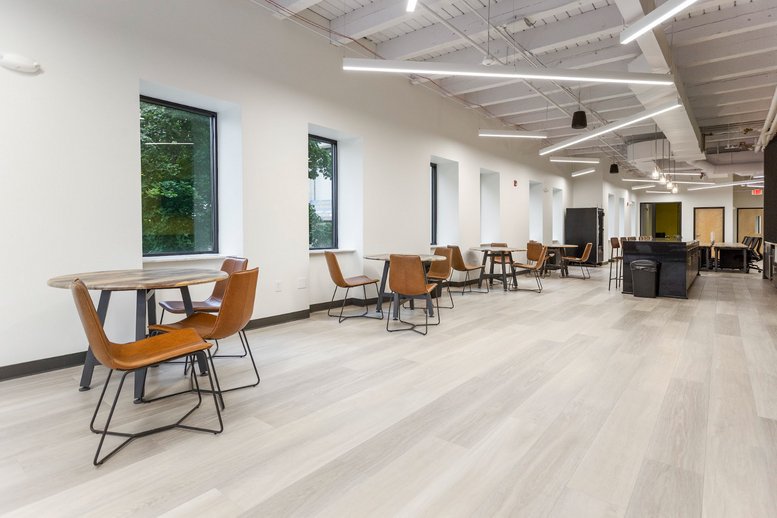 Breakout area with round café tables, tan chairs, and industrial ceiling.