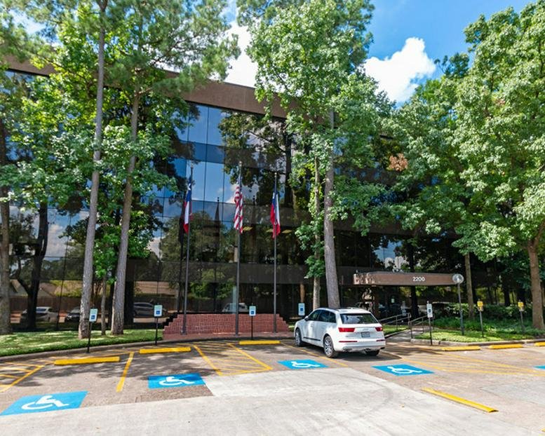 Exterior view of the professional glass building at 2200 North Loop West surrounded by mature trees.