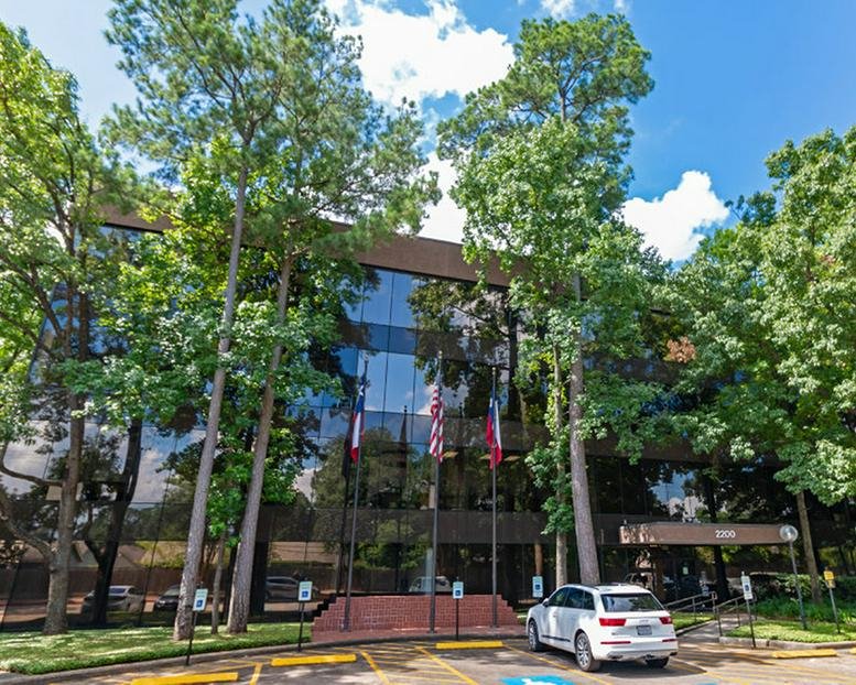 Exterior view of the glass-facade building at 2200 North Loop West with flags and mature trees.