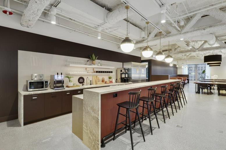 Lively communal kitchen area at The Franklin with a long wooden bar, pendant lights, and espresso machine.