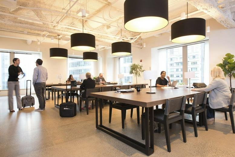 Spacious coworking lounge at The Franklin with large drum pendant lights and wooden tables.
