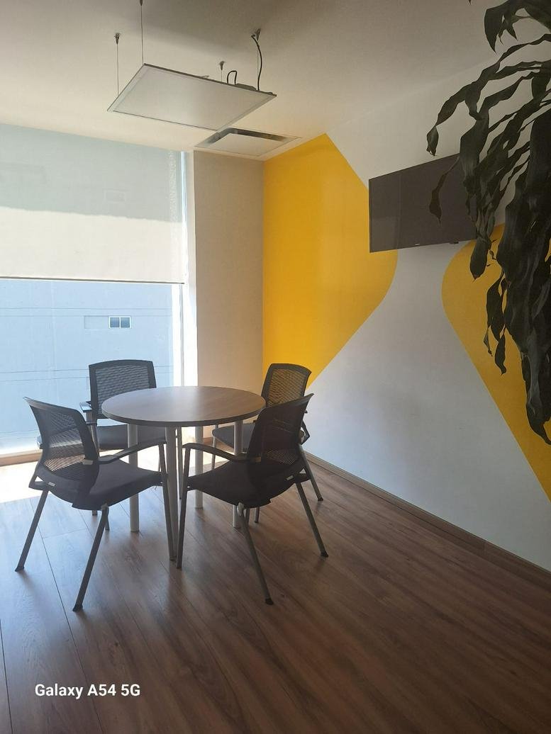 Small meeting area with a round table, four chairs, and a yellow feature wall.