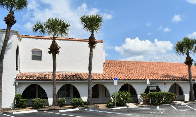 Exterior view of the Mediterranean-style building at 2431 Aloma Ave, Winter Park featuring palm trees and a tiled roof.