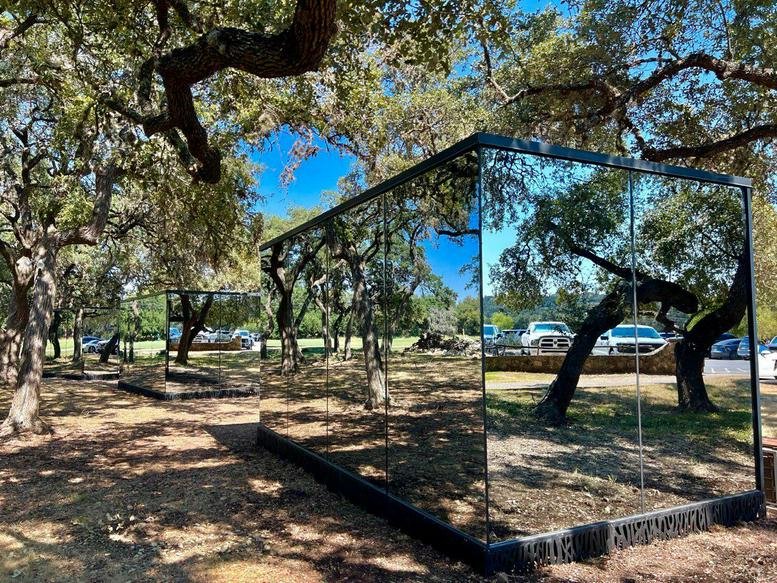 Mirrored exterior of a modern office pod reflecting surrounding oak trees.