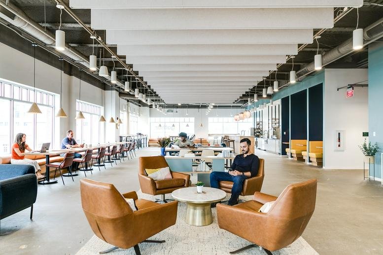 Vibrant communal lounge area with leather armchairs, coffee table, and acoustic ceiling panels.