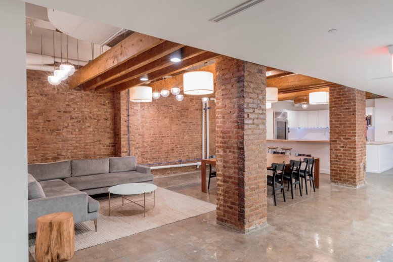 Spacious lounge with exposed brick walls, timber beams, a grey sectional sofa, and a dining table.
