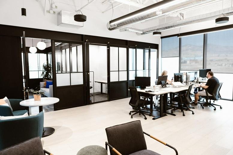 Spacious lounge and breakout area with modern furniture, glass-walled offices, and large windows.