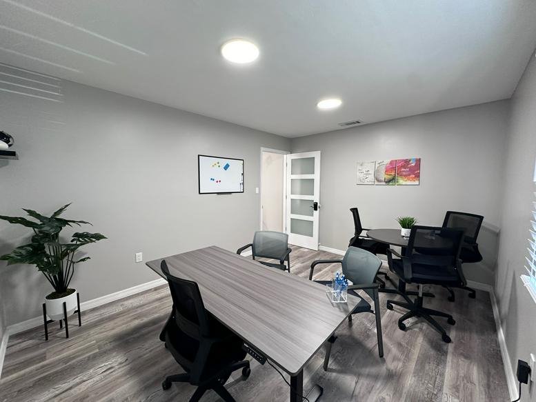 Meeting room with a grey wood grain table, black mesh chairs, and a large potted plant.
