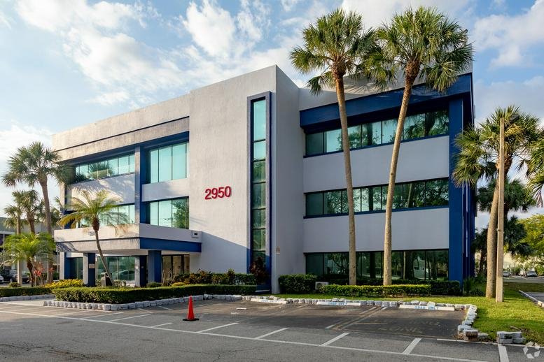 Exterior view of the white and blue office building at 2950 W. Cypress Creek Rd with palm trees.