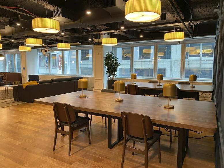 Bright communal coworking space with wood floors, warm hanging lamps, and a lounge area.