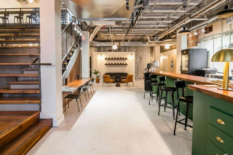 Spacious open-plan lounge with industrial ceiling, wooden stairs, and a green counter.
