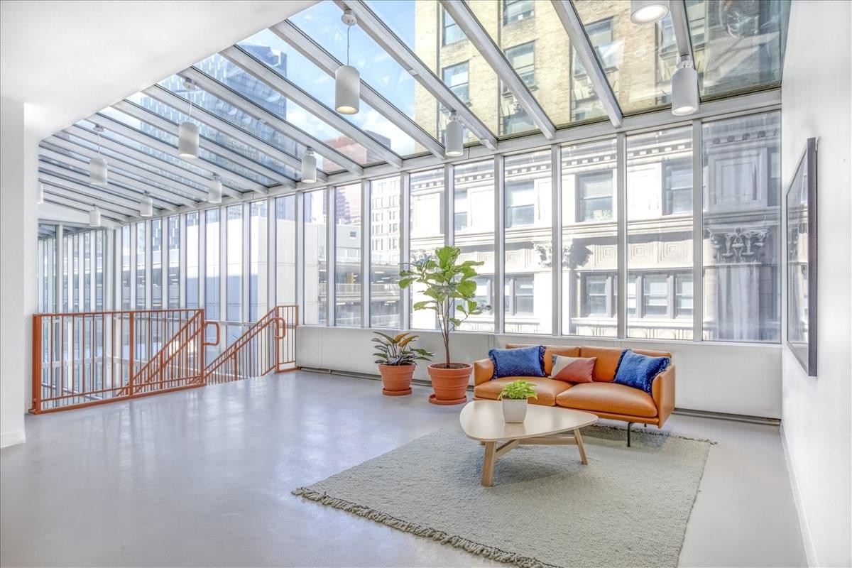 Sunlit lounge area with an orange leather sofa and a glass-paneled ceiling.
