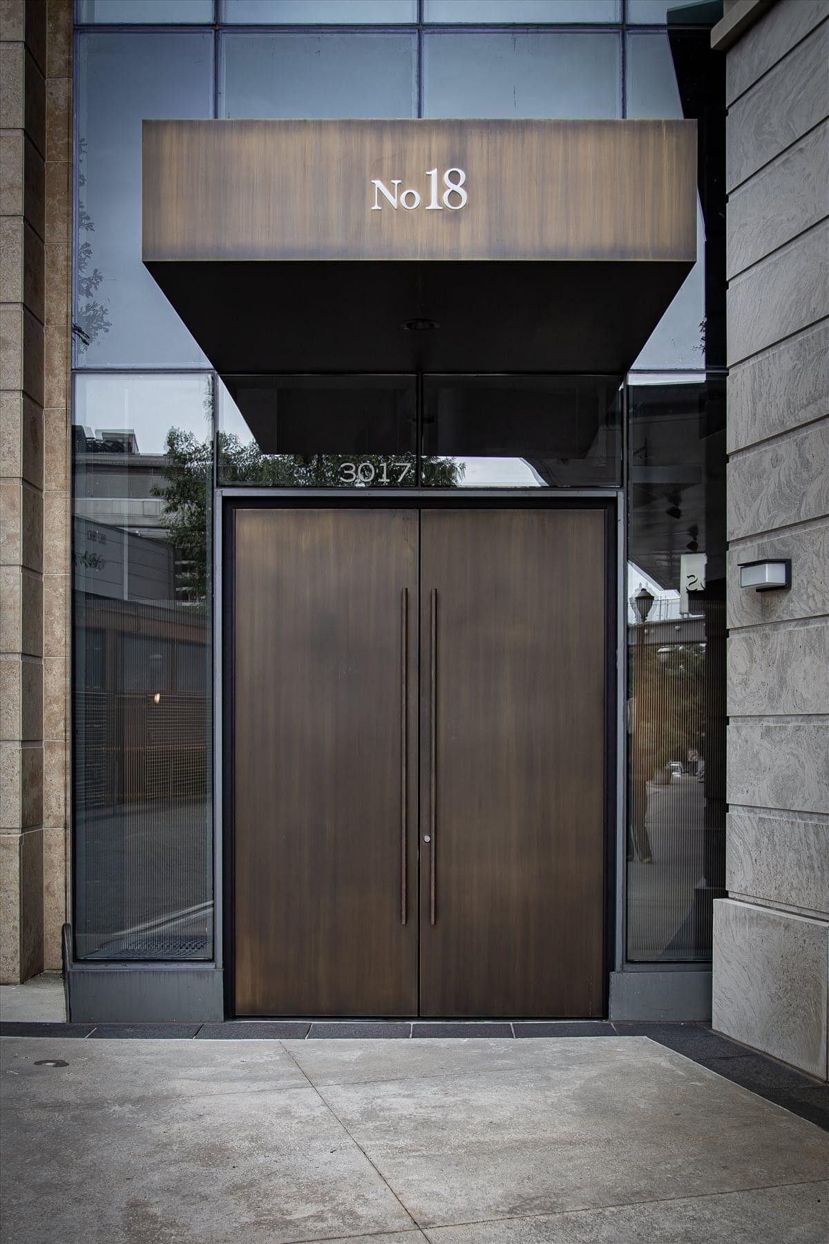 Sleek brass-finished double doors under a No 18 building entrance canopy.