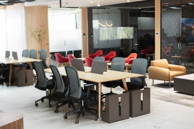 Spacious communal coworking lounge at 3040, Avenida México, Guadalajara with colorful chairs and wooden tables.