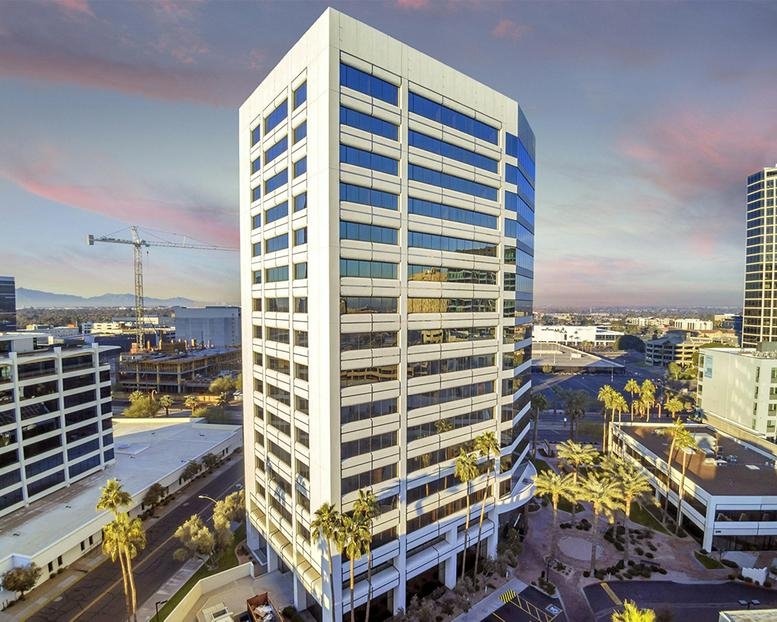 Aerial view showing the full height of the modern office tower under a sunset sky.