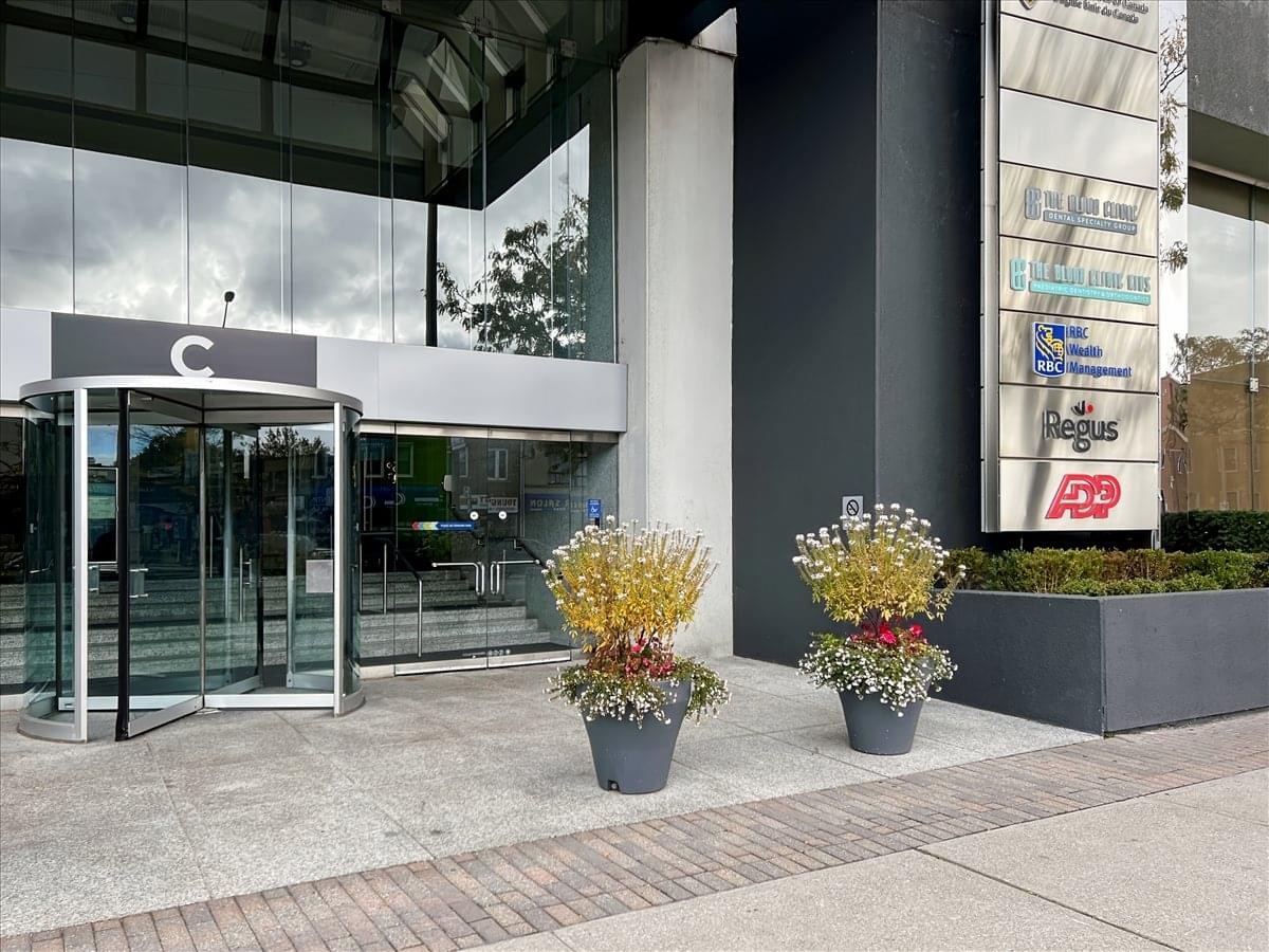 Exterior entrance of 3250 Bloor Street West featuring revolving glass doors and floral planters.