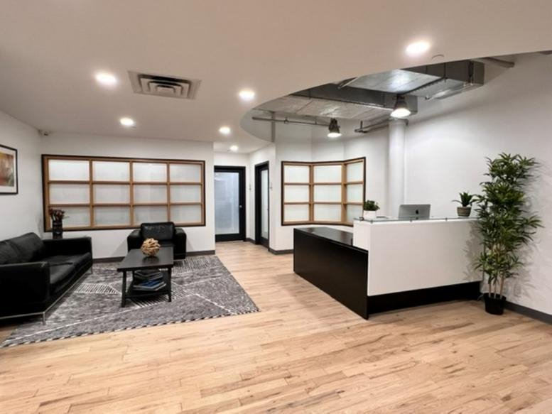 Spacious reception area with wooden floors, black sofa, and a modern white front desk.