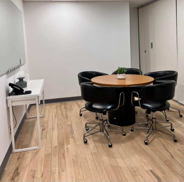 Small breakout room with a round wooden table, black swivel chairs, and wood flooring.