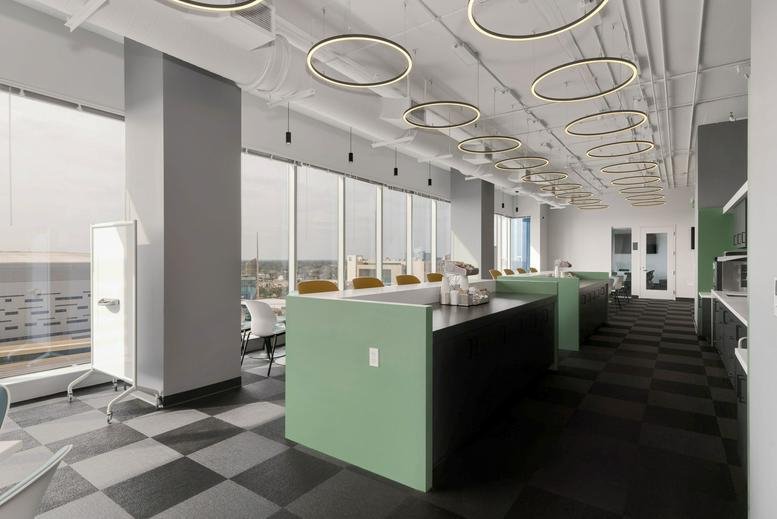 Open-plan coworking area with green-walled booths, checkered flooring, and circular pendant lights.